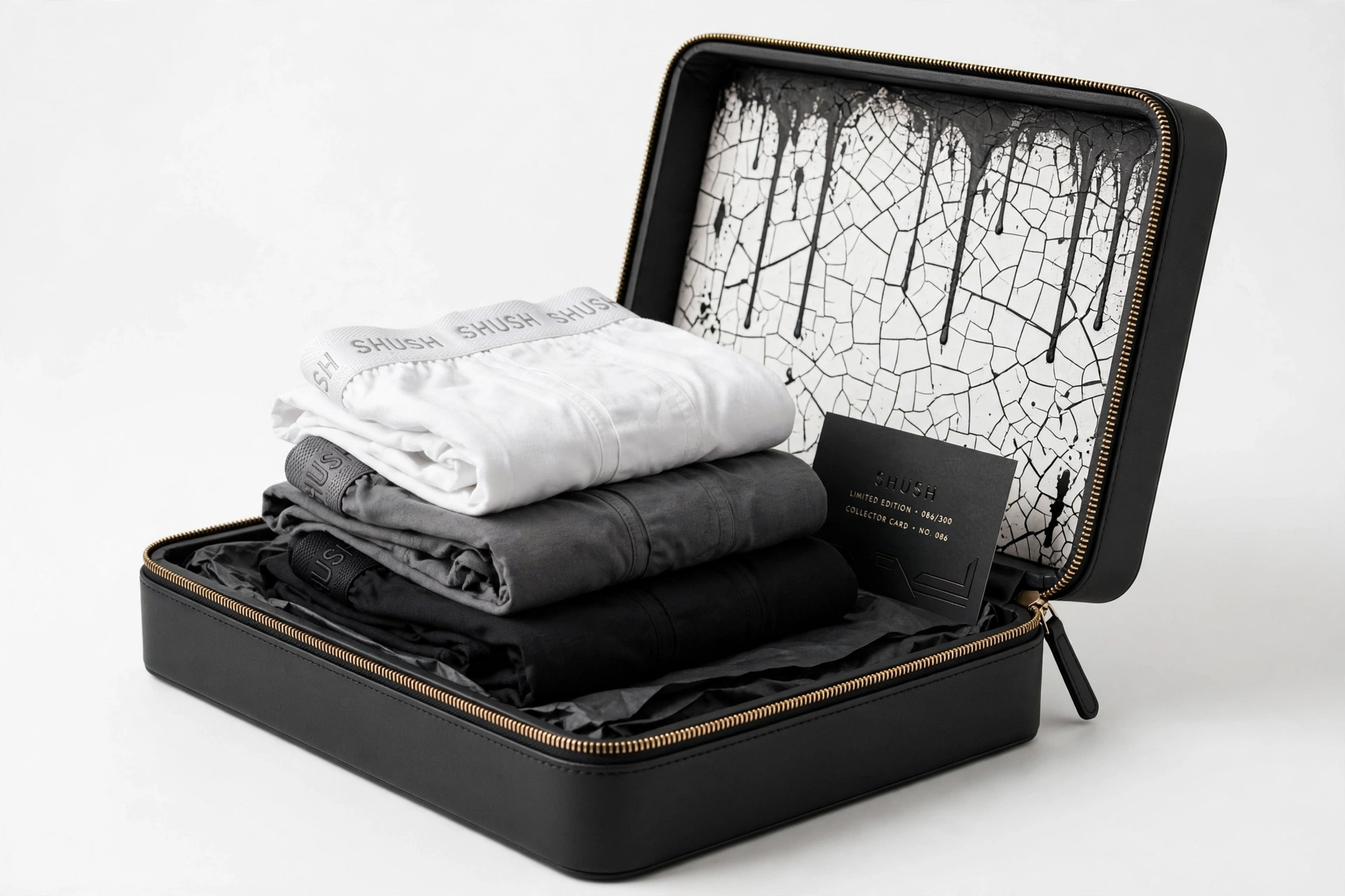 Three pairs of SHUSH fitted boxer briefs in white, charcoal and black stacked inside the matte black zippered keepsake case with a numbered collector card