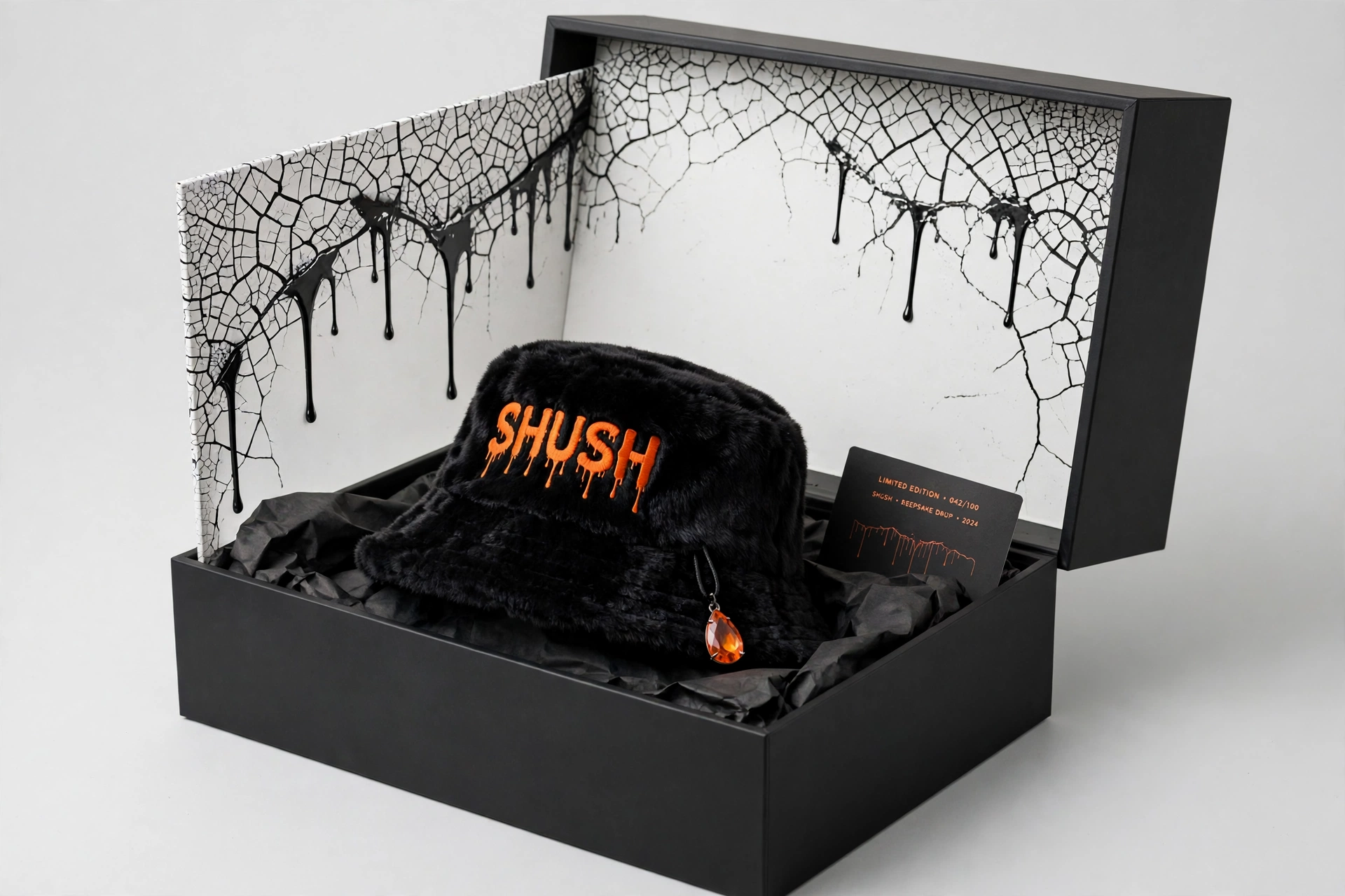 Black faux-fur SHUSH bucket hat with an amber gem drop inside its black keepsake box with cracking-print lining and a numbered collector card