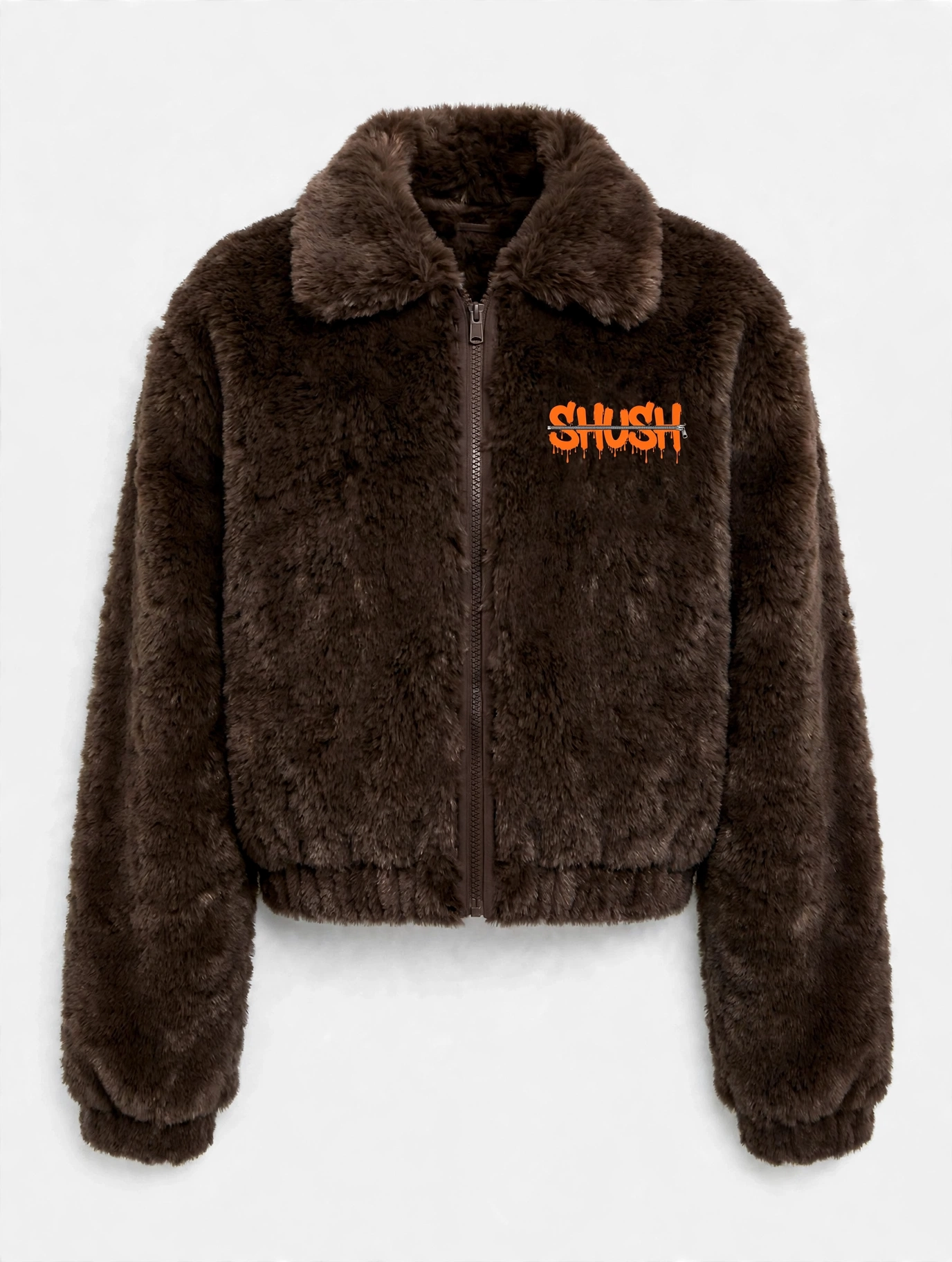 Women's cropped dark brown faux-fur jacket, front view — plush fur, zip front, and a small embroidered SHUSH mark at the left shoulder: the word SHUSH in orange dripping letters zipped shut by a silver zipper